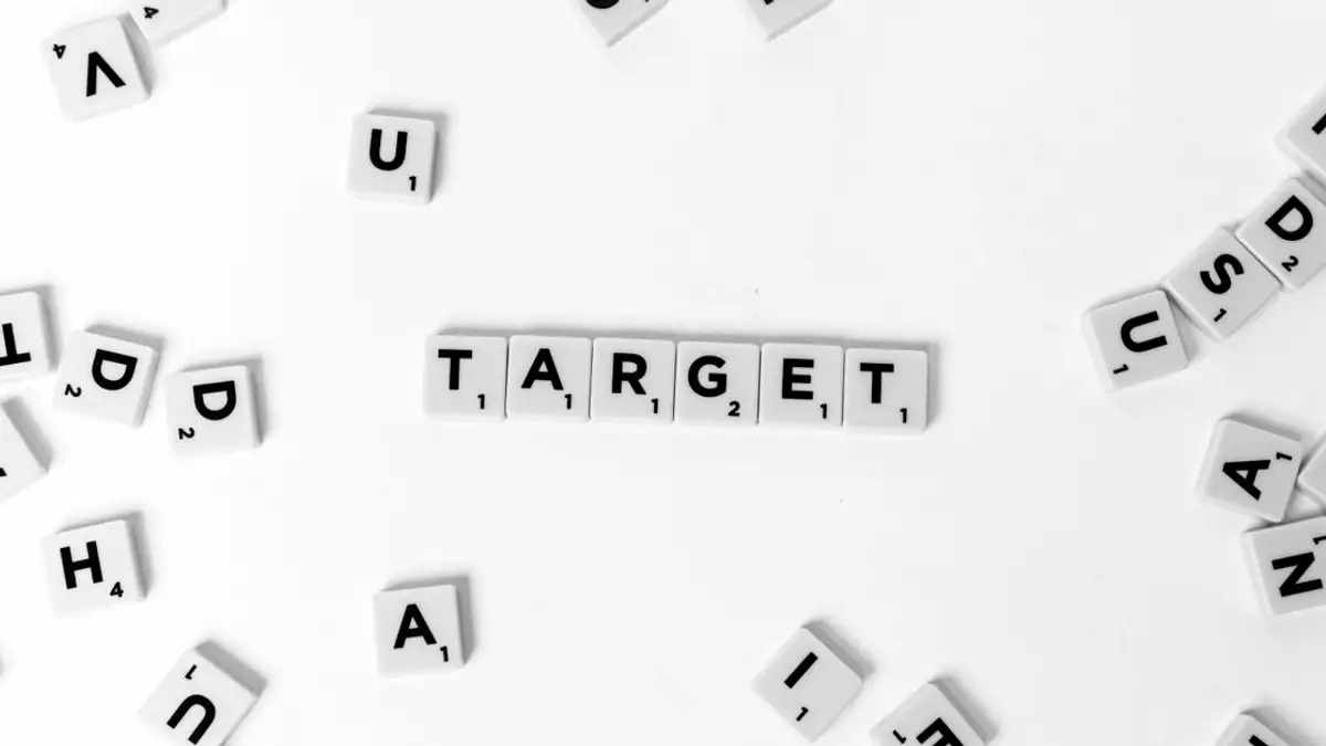 Kumpulan ubin Scrabble yang disusun untuk mengeja 'Sasaran' di antara huruf-huruf yang tersebar di latar belakang putih.