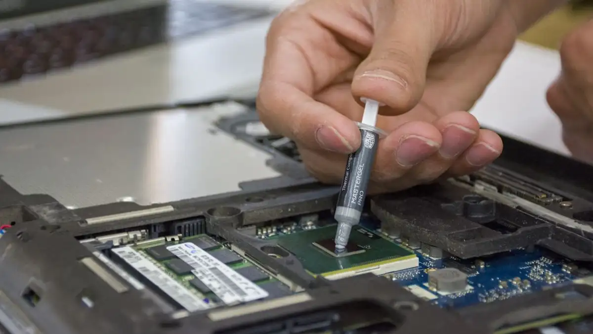 Close-up tangan yang mengoleskan pasta termal pada mikrochip laptop untuk perawatan.
