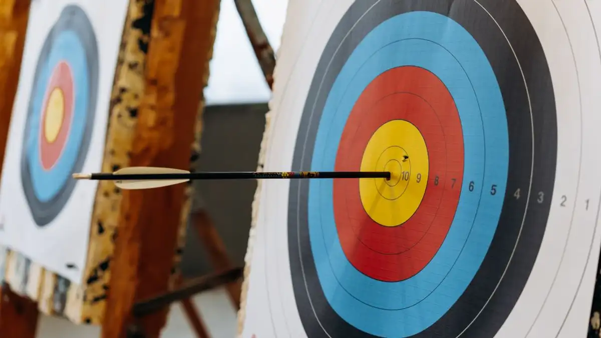 Sebuah panah mengenai pusat target di arena panahan dalam ruangan yang berwarna-warni.