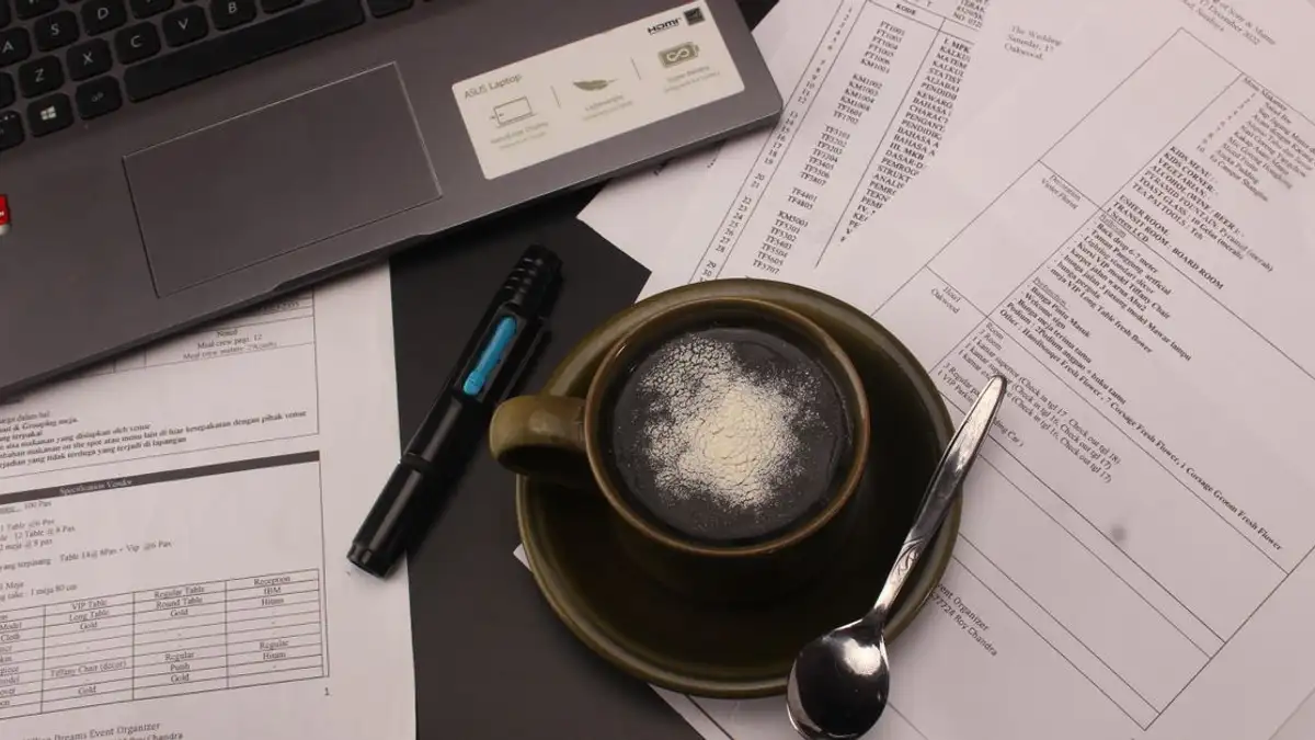 Tampilan dekat sebuah meja dengan secangkir kopi, dokumen, dan laptop untuk sesi kerja yang produktif.