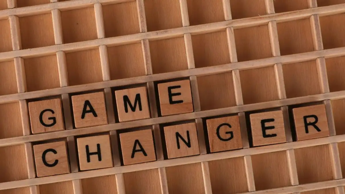 Ubin Scrabble membentuk 'Game Changer' di atas kisi kayu, melambangkan inovasi atau transformasi.