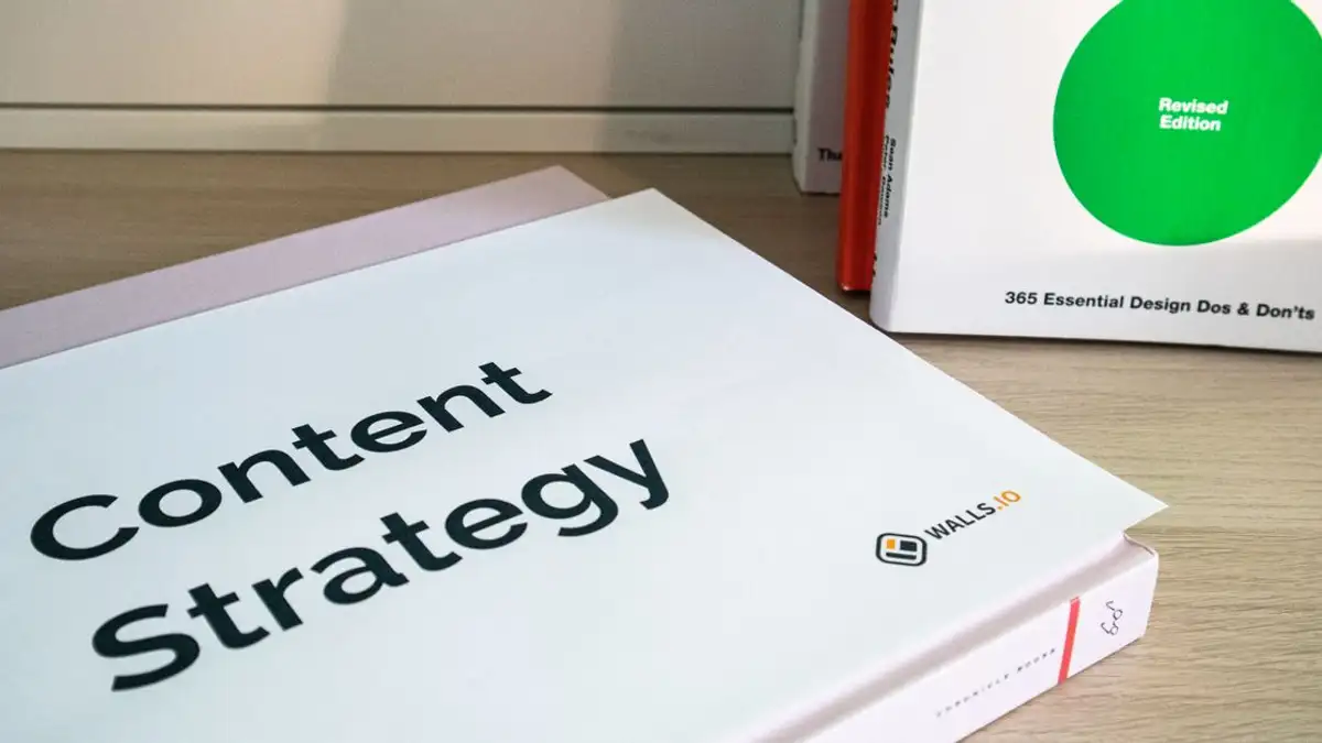 Buku tentang strategi konten dan dasar-dasar desain grafis yang terletak di meja kayu.
