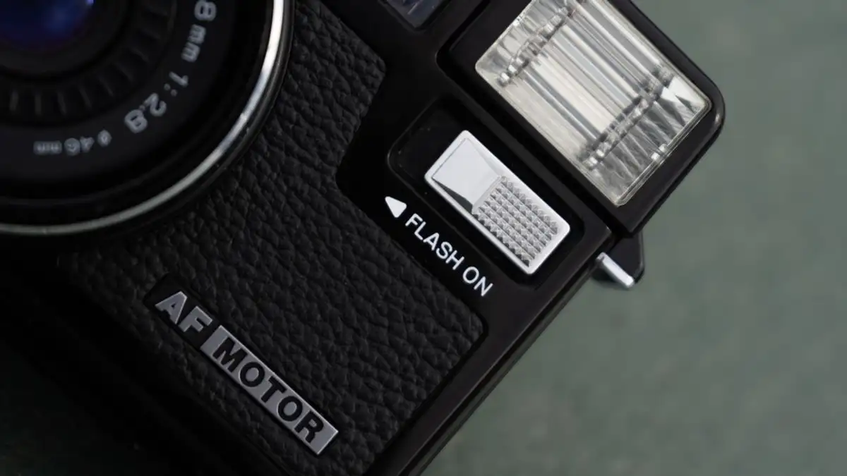 Tampilan detail jarak dekat dari kamera film vintage dengan lampu kilat menyala, menampilkan gaya dan desain klasik.
