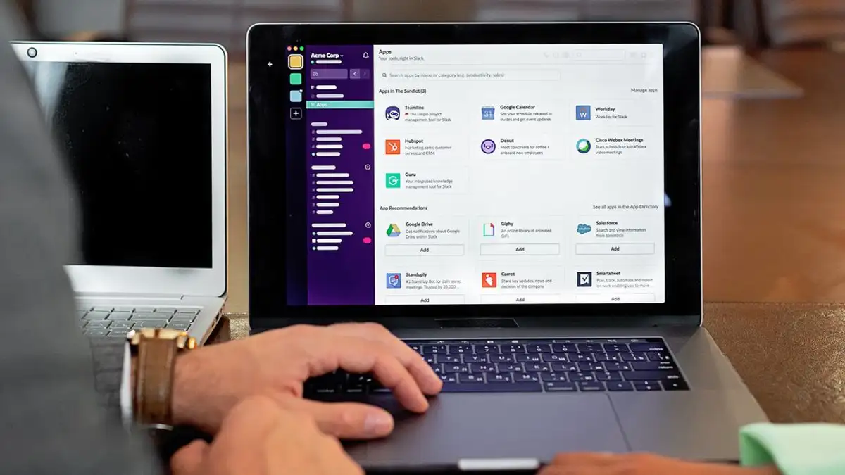 Dua profesional berkolaborasi menggunakan laptop dan perangkat lunak komunikasi dalam lingkungan bisnis.