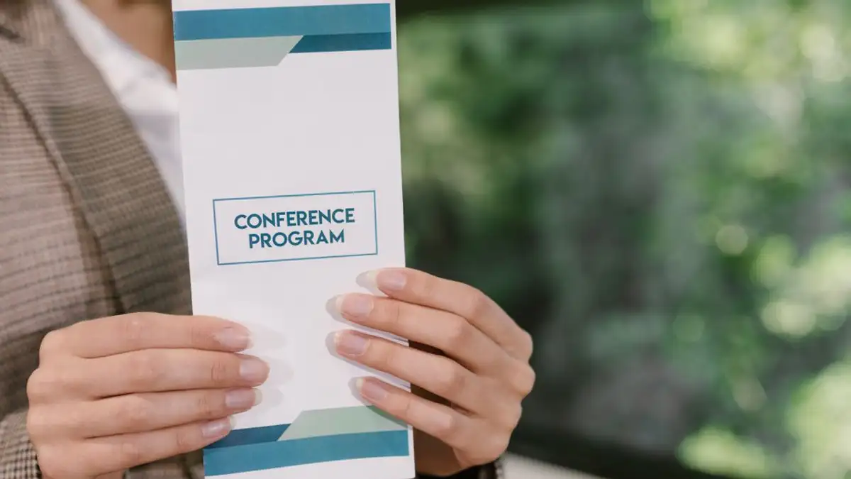 Seorang profesional memegang brosur program konferensi, siap untuk para peserta acara.