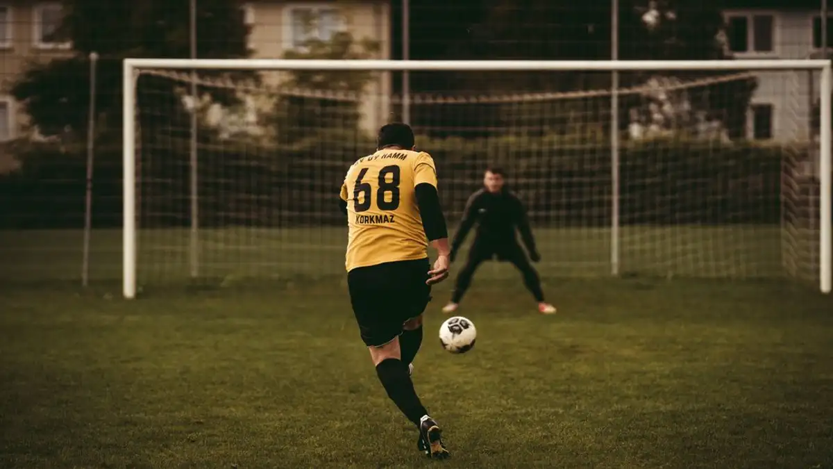 Seorang pemain sepak bola mengambil tendangan penalti yang menentukan dengan tujuan mencetak gol melawan kiper.