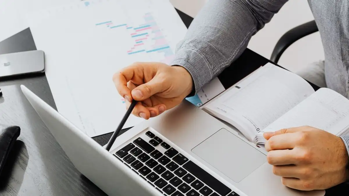 Profesional menggunakan laptop dan meninjau dokumen di meja kantor untuk analisis data.