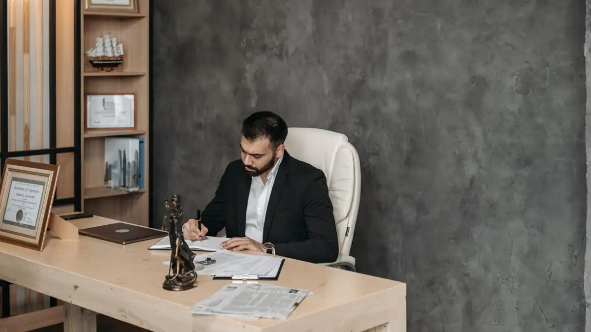 Pengusaha dalam setelan menulis di meja di lingkungan kantor modern.