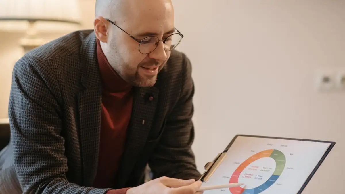 Seorang pria menjelaskan data menggunakan grafik berkode warna di clipboard dalam suasana indoor yang nyaman.