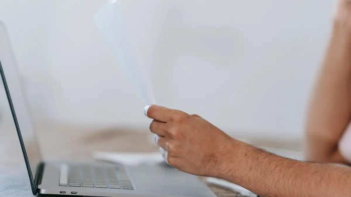 Seorang pria melakukan multitasking, berbicara di telepon dan meninjau dokumen sambil bekerja di laptop di dalam ruangan.