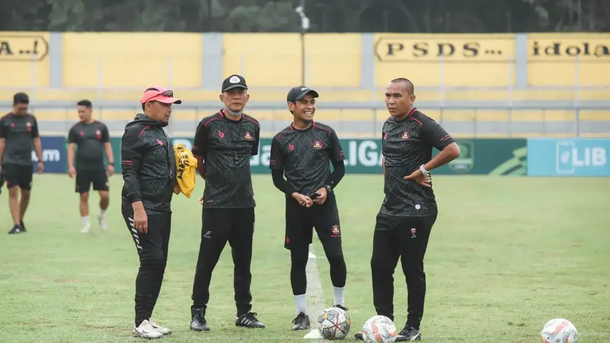 Sekelompok pelatih Indonesia berdiskusi di lapangan sepak bola di siang hari.
