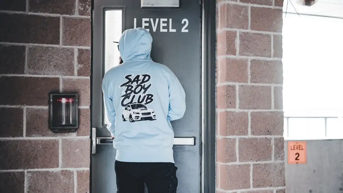 Individu dalam hoodie biru menghadap pintu yang bertuliskan 'Level 2' di lingkungan perkotaan.