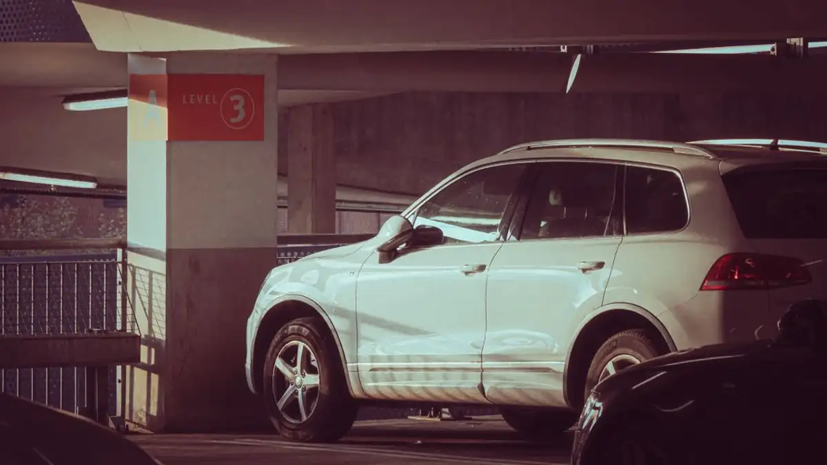 SUV putih diparkir di garasi multi-lantai di level 3 dengan sinar matahari menciptakan bayangan modern.